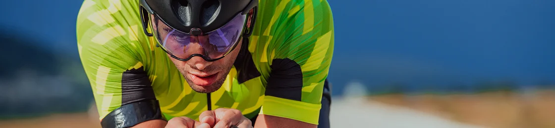 Un cycliste vêtu d'un maillot vert vif et d'un casque noir se concentre intensément tout en roulant sur une route dégagée sous un ciel bleu profond, exprimant détermination et vitesse.