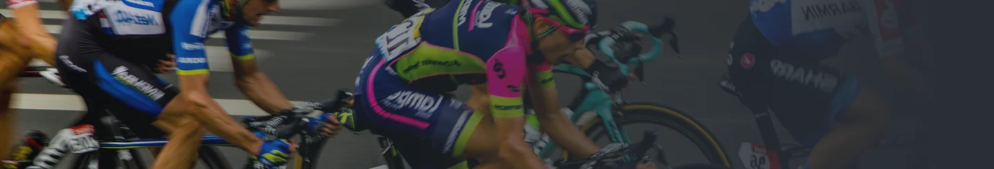 Des cyclistes vêtus de maillots aux couleurs vives roulent à toute vitesse sur une route, penchés en avant avec détermination. L'arrière-plan est flou, ce qui donne une impression de vitesse et de mouvement.